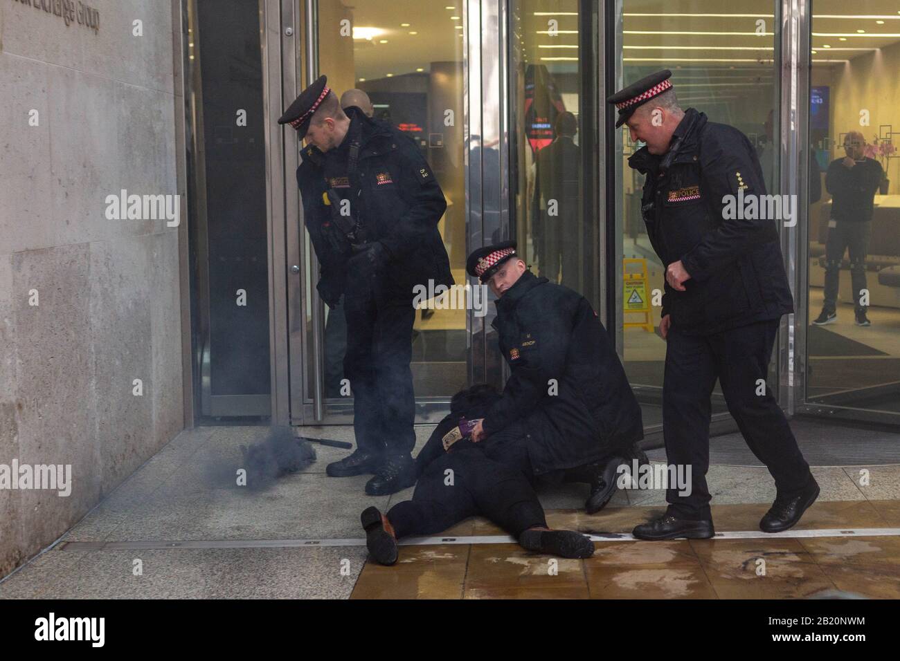 Londra, Regno Unito. 28 febbraio 2020. Un attivista è trattenuto dagli agenti di polizia fuori dalla Borsa di Londra a Paternoster Square durante una protesta che coinvolge gruppi anarchici e anti-capitalisti. La dimostrazione mette in evidenza le critiche sistemiche del capitalismo e del collasso ecologico, con fumo visibile che suggerisce interruzioni o misure di controllo della folla. Penelope Barritt/Alamy Live News Foto Stock