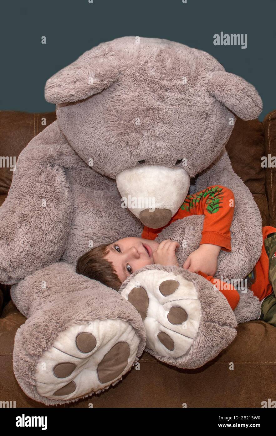 Ragazzo sorridente con orso gigante mentre si trova in grembo Foto Stock