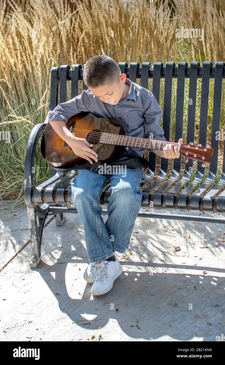 Un giovane ragazzo pratica la sua chitarra acustica all'aperto in una bella giornata autunnale Foto Stock