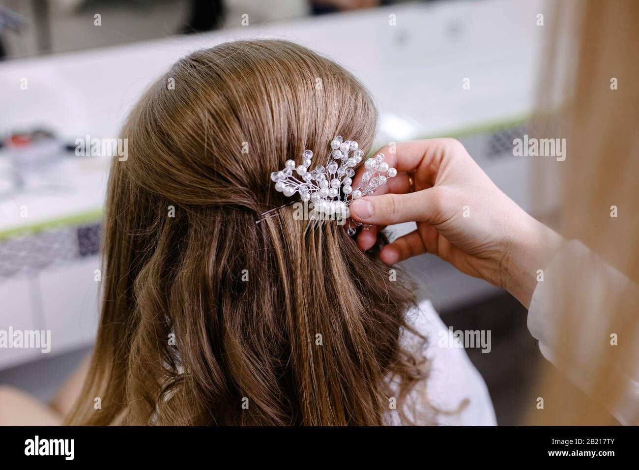 Vista posteriore a pettinatura con tornante. Parrucchiere che fa acconciatura di nozze a donna bionda capelli con capelli lunghi in salone di bellezza. Cura professionale dei capelli Foto Stock