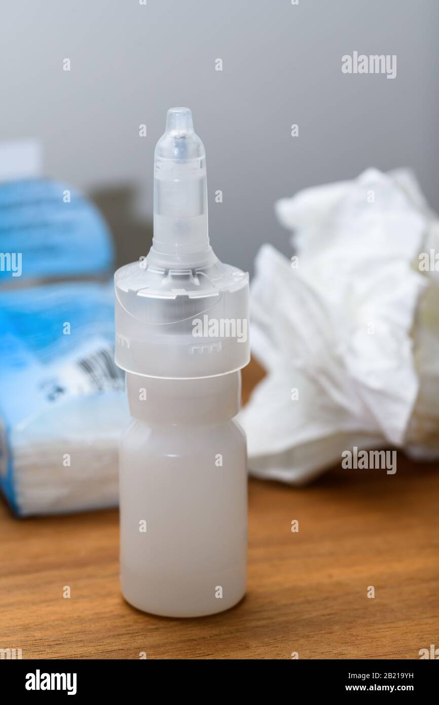 Primo piano del flacone spray nasale e del tessuto di carta su un comodino utilizzato durante raffreddore, influenza o virus.Concetto per le condizioni mediche all'interno della casa. Foto Stock