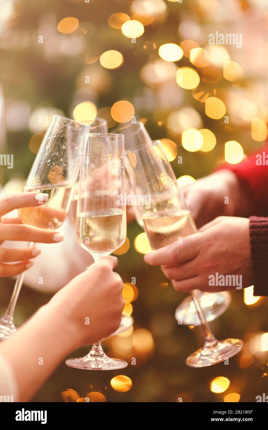 Crop mani di uomini e donne senza volto bicchieri di champagne con bella verde albero di Natale su sfondo sfocato Foto Stock