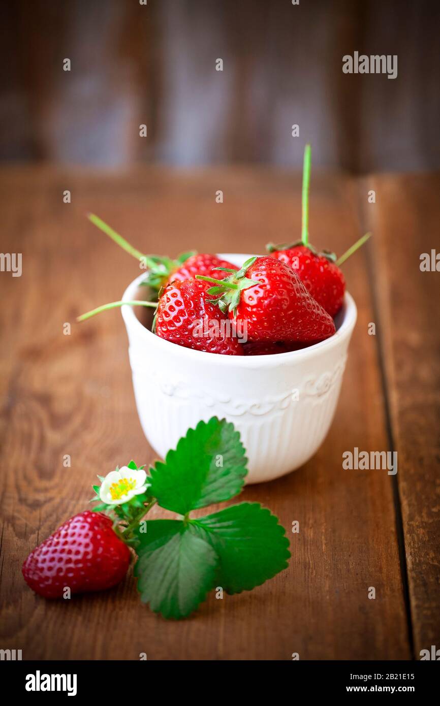 Fragole rosse mature con foglie verdi in ciotola bianca su tavola di legno Foto Stock