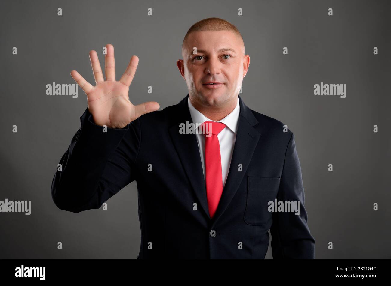 Ritratto di uomo d'affari fresco che indossa elegante abito nero e cravatta rossa che mostra cinque isolati su sfondo grigio Foto Stock