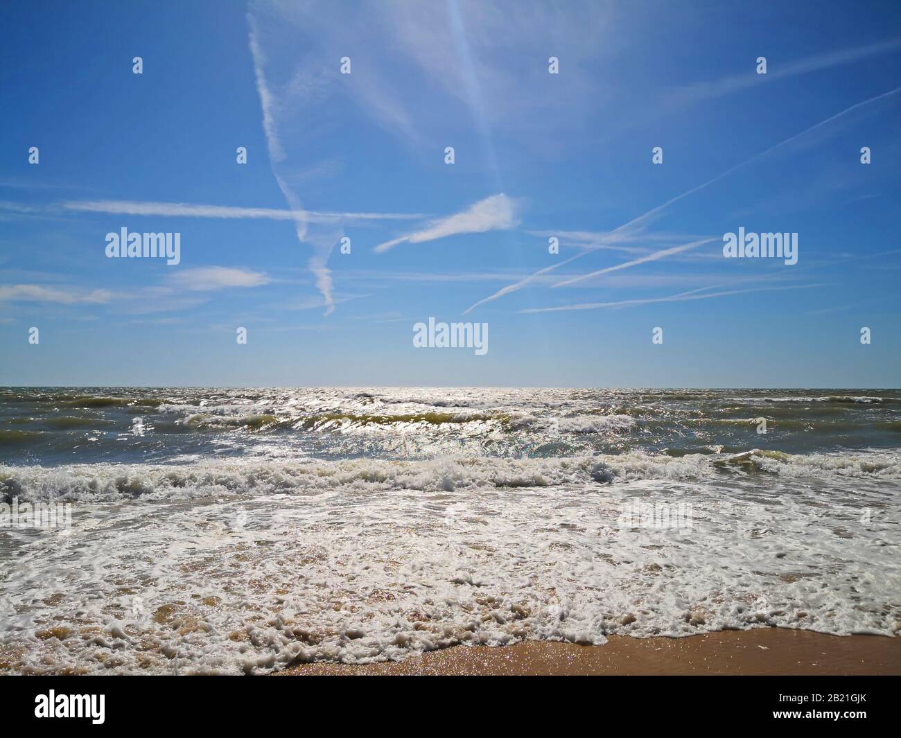 Schiuma bianca di onde al mare, ampio cielo blu con tracce bianche. Estate, Matalascanas, Spagna Foto Stock