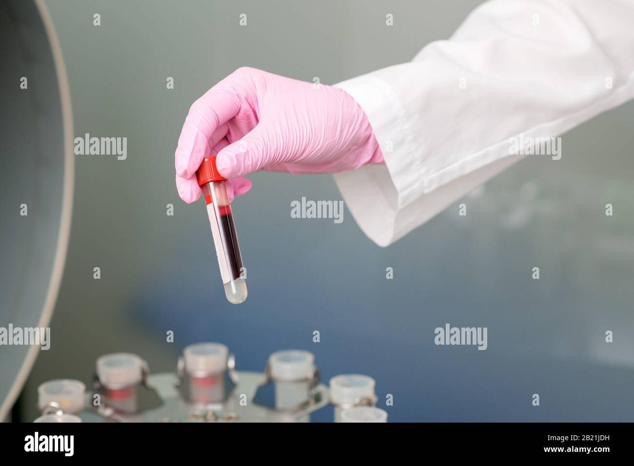 Guanto a mano del medico con provetta per analisi del sangue su sfondo centrifuga. Foto Stock