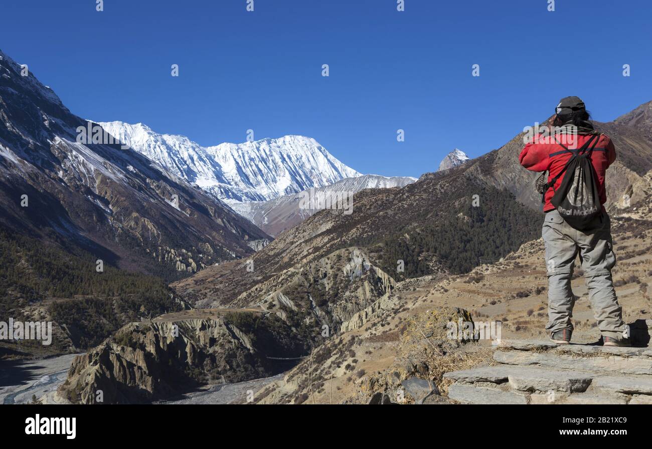 L'uomo del Nepal locale ammira le vedute del paesaggio di Cime Innevate Distanti sul circuito Annapurna Escursionismo e Trekking Trail in Himalaya Mountains Foto Stock