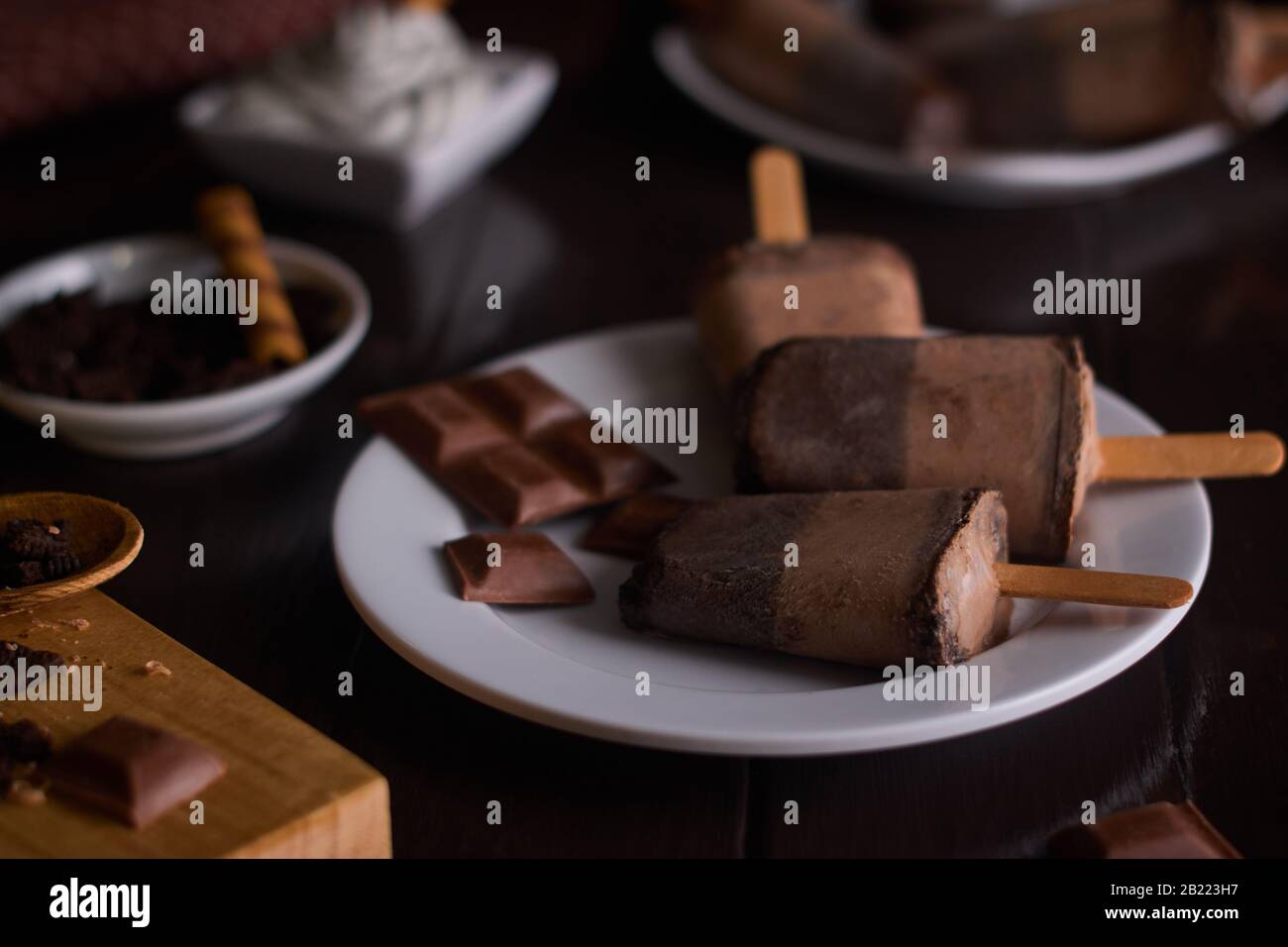 Gelato al cioccolato e biscotto su una tazza di ceramica bianca con fondo di legno marrone con pezzi di cioccolato e biscotti Foto Stock