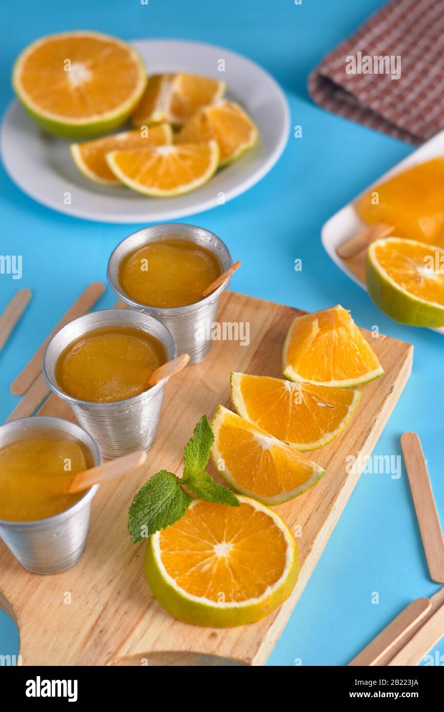 Gelato all'arancia e alla menta piperita con pezzi d'arancia su tagliere in legno con sfondo azzurro Foto Stock