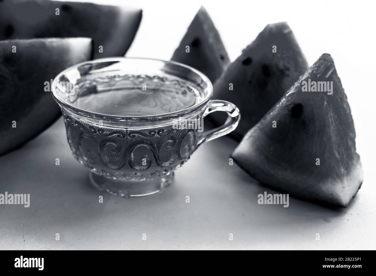 Tè disintossicante di semi di melone in una tazza di vetro trasparente insieme a pezzi di cocomero in forma triangolare isolati su bianco. Foto Stock