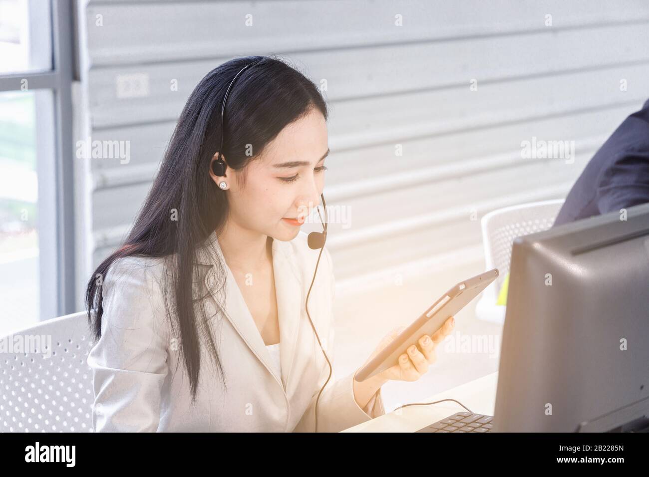 L'operatore di un call center asiatico femminile guarda un tablet digitale incandescente. Concetto di servizio di assistenza clienti, stile di vita in ufficio, dipendente. Foto Stock