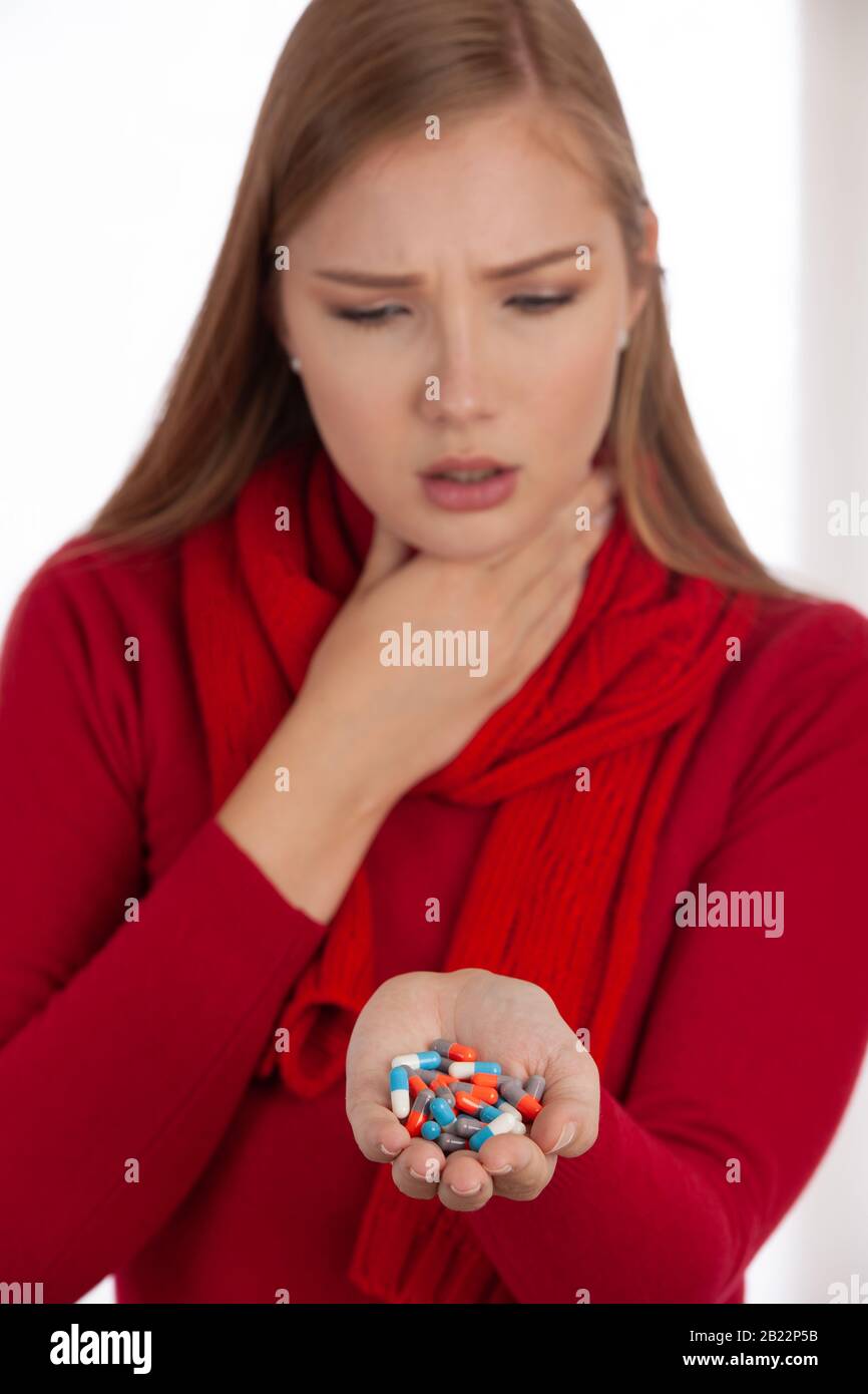 Giovane donna in maglione rosso tiene le pillole nella sua mano come lei è ammalata Foto Stock