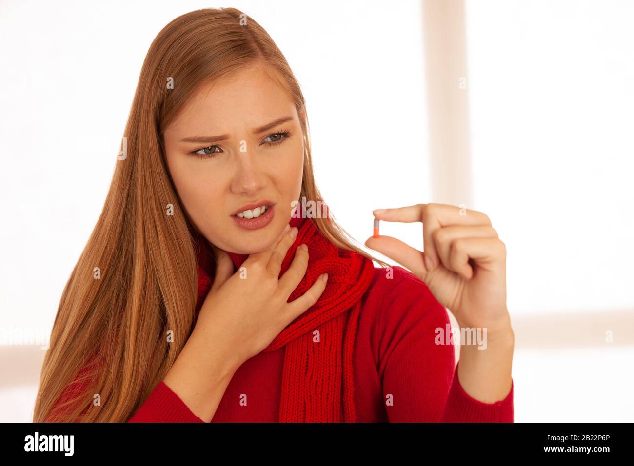 Giovane donna in maglione rosso tiene le pillole nella sua mano come lei è ammalata Foto Stock