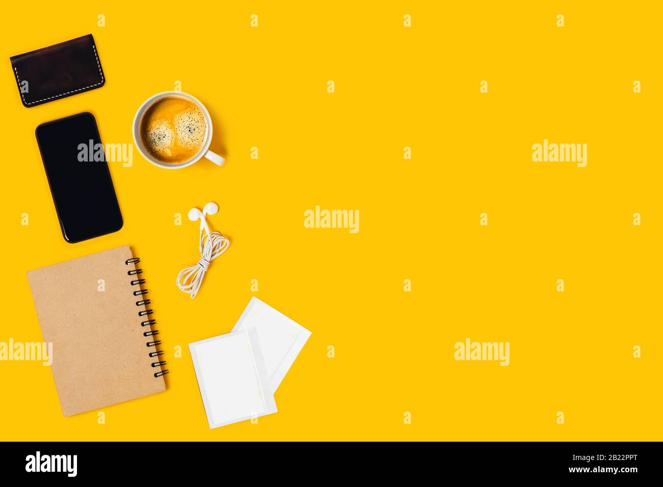 Desktop da ufficio su sfondo giallo con smartphone, blocco note, caffè, immagine polaroide, cuffie. Foto Stock