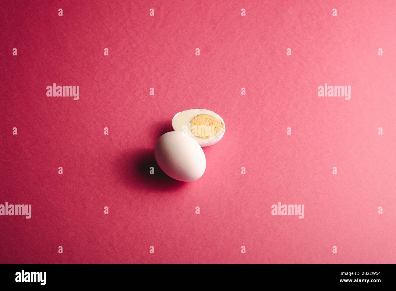 Uovo bianco vicino a uova sode bollite su rosa rosso colori pianura sfondo minimo, angolo di vista, felice giorno di Pasqua Foto Stock