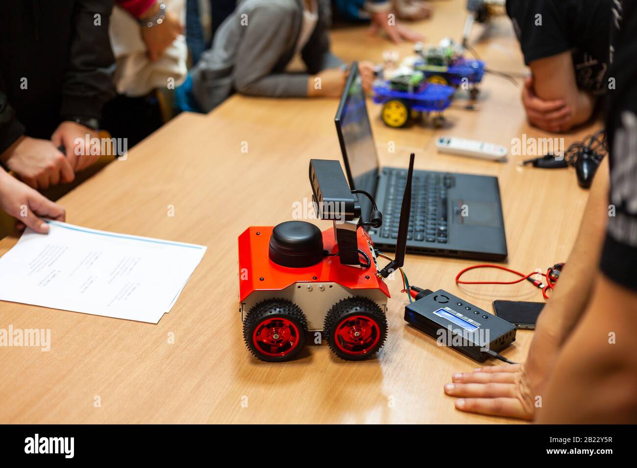 Robotica, robot fai da te a quattro ruote con antenna, laptop sul tavolo, persone riunite in giro, meeting tecnico, presentazione. Ingegneria meccanica semplice Foto Stock