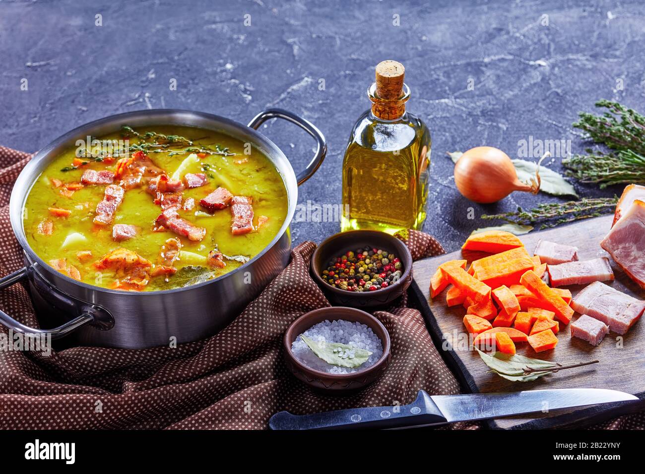 Classica stufato di piselli tedeschi con erbsensupe con pancetta, prosciutto di maiale, carota, patate con timo - piatto invernale abbondante servito su una pentola su fondo di cemento, olive Foto Stock