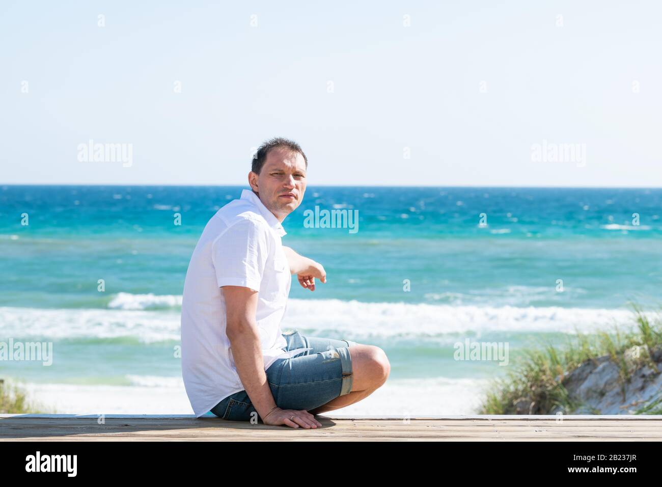 Lungomare, Florida terrazza Boardwalk durante la giornata di sole in panhandle villaggio spiaggia con oceano e orizzonte e uomo seduto infelice puntamento verso l'oceano Foto Stock