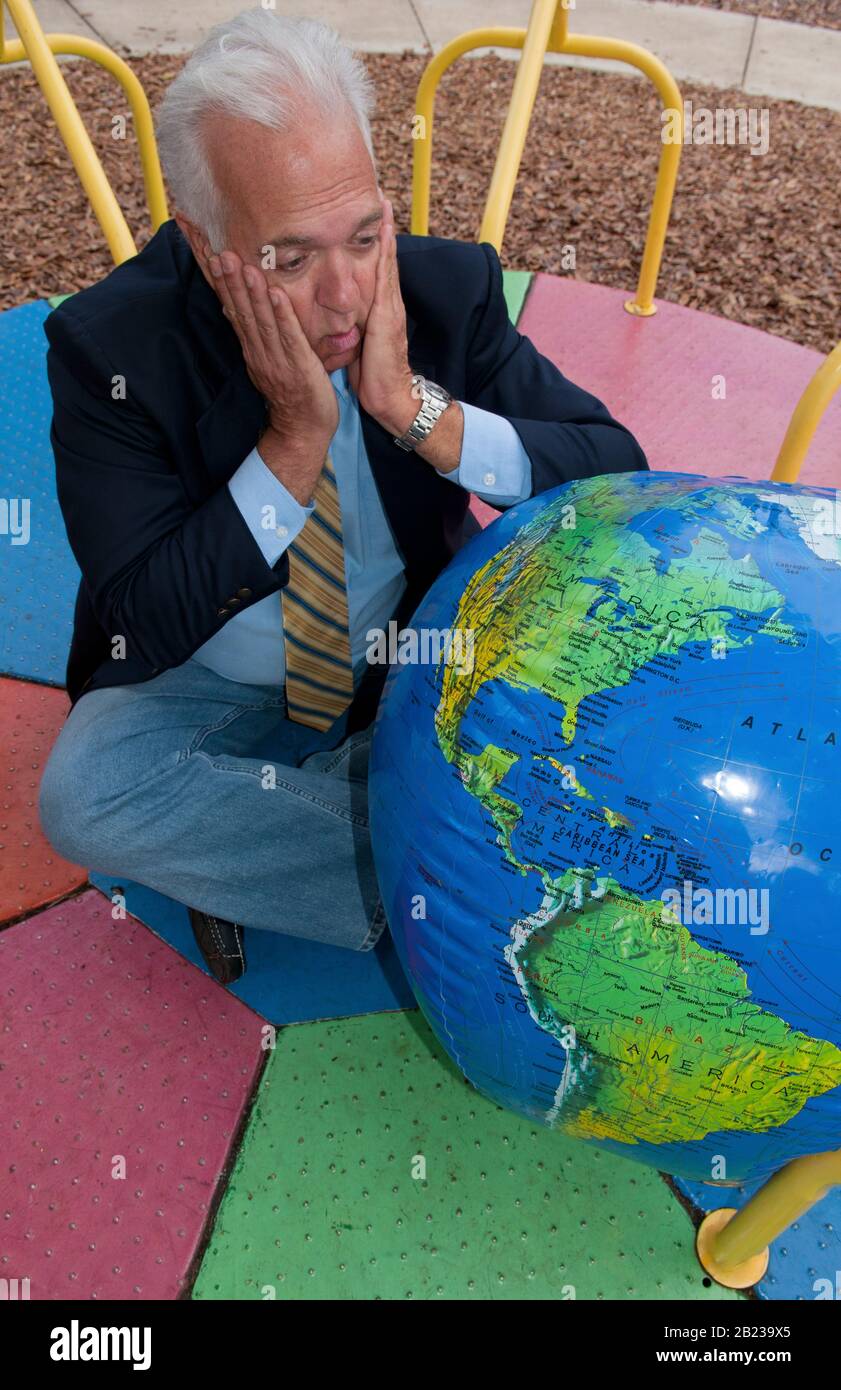 Unentschlossener Mann sitzt vor Weltkugel und schmiedet Reiseplaene, MR: Si Foto Stock