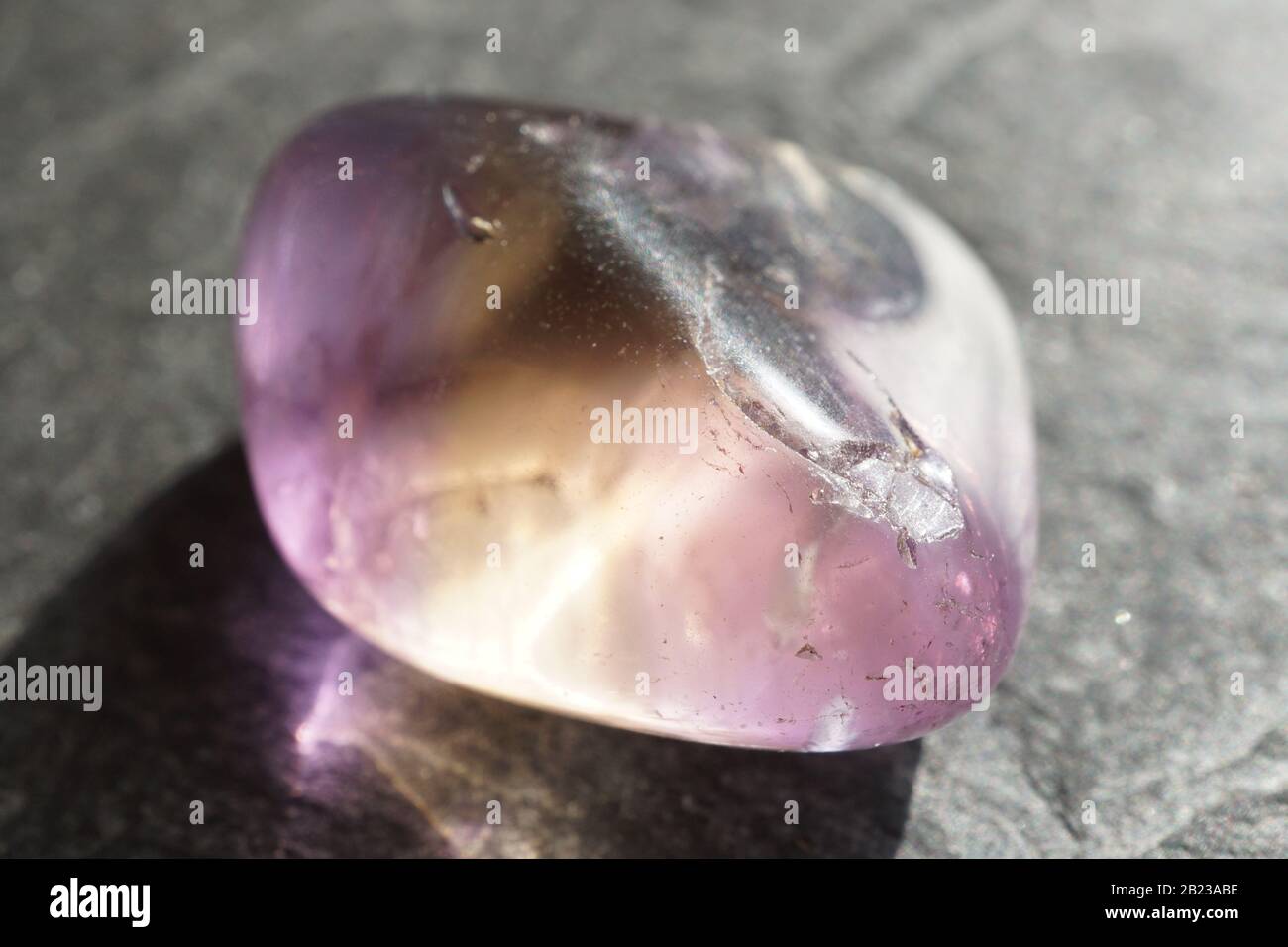 Ametrina tumbled ghiaia su sfondo grigio ardesia, illuminato dal sole Foto Stock