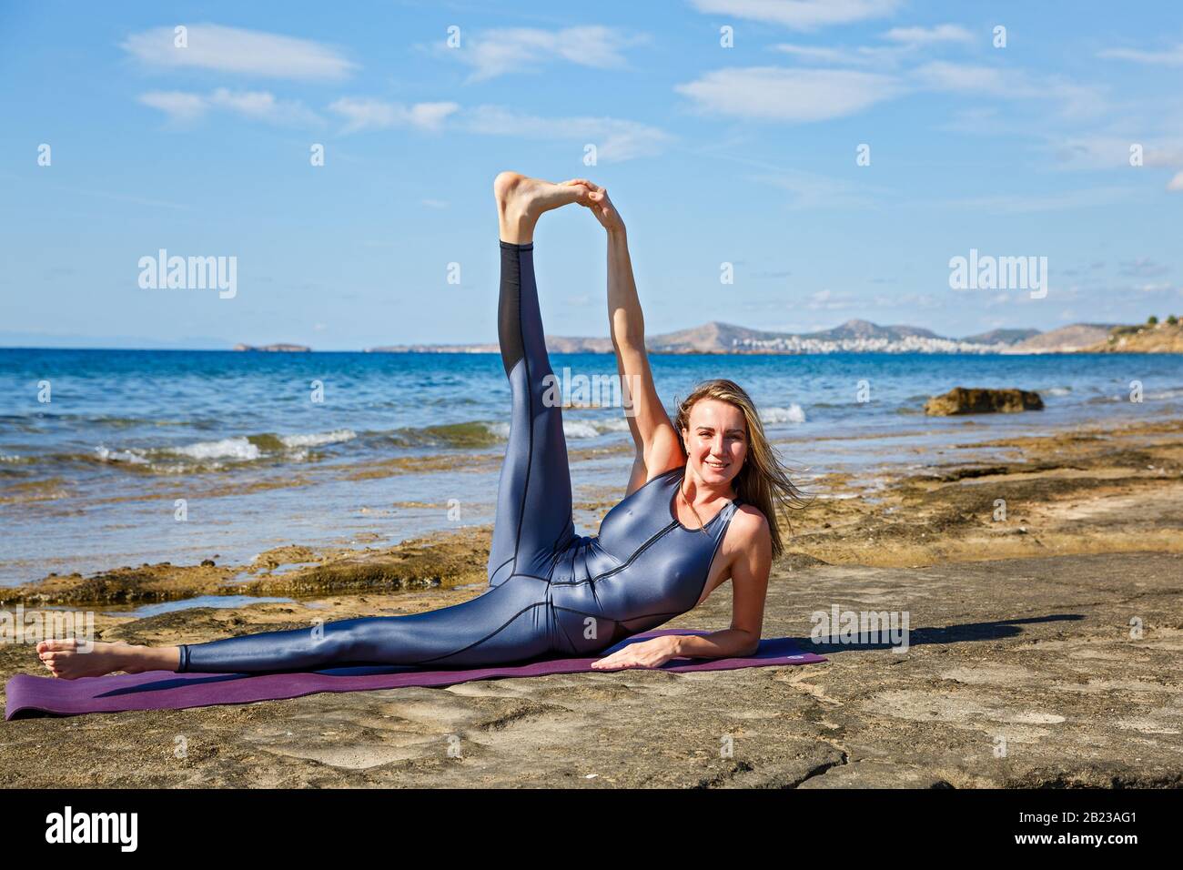 Giovane bella donna in una tuta facendo esercizi sportivi sulla spiaggia. Foto Stock