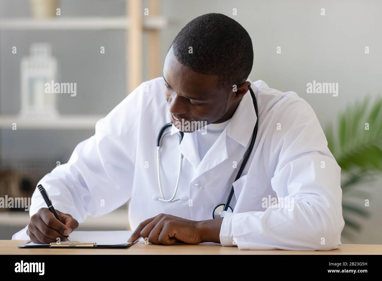 Il medico africano americano serio che riempie il documento del modulo del paziente si chiude Foto Stock