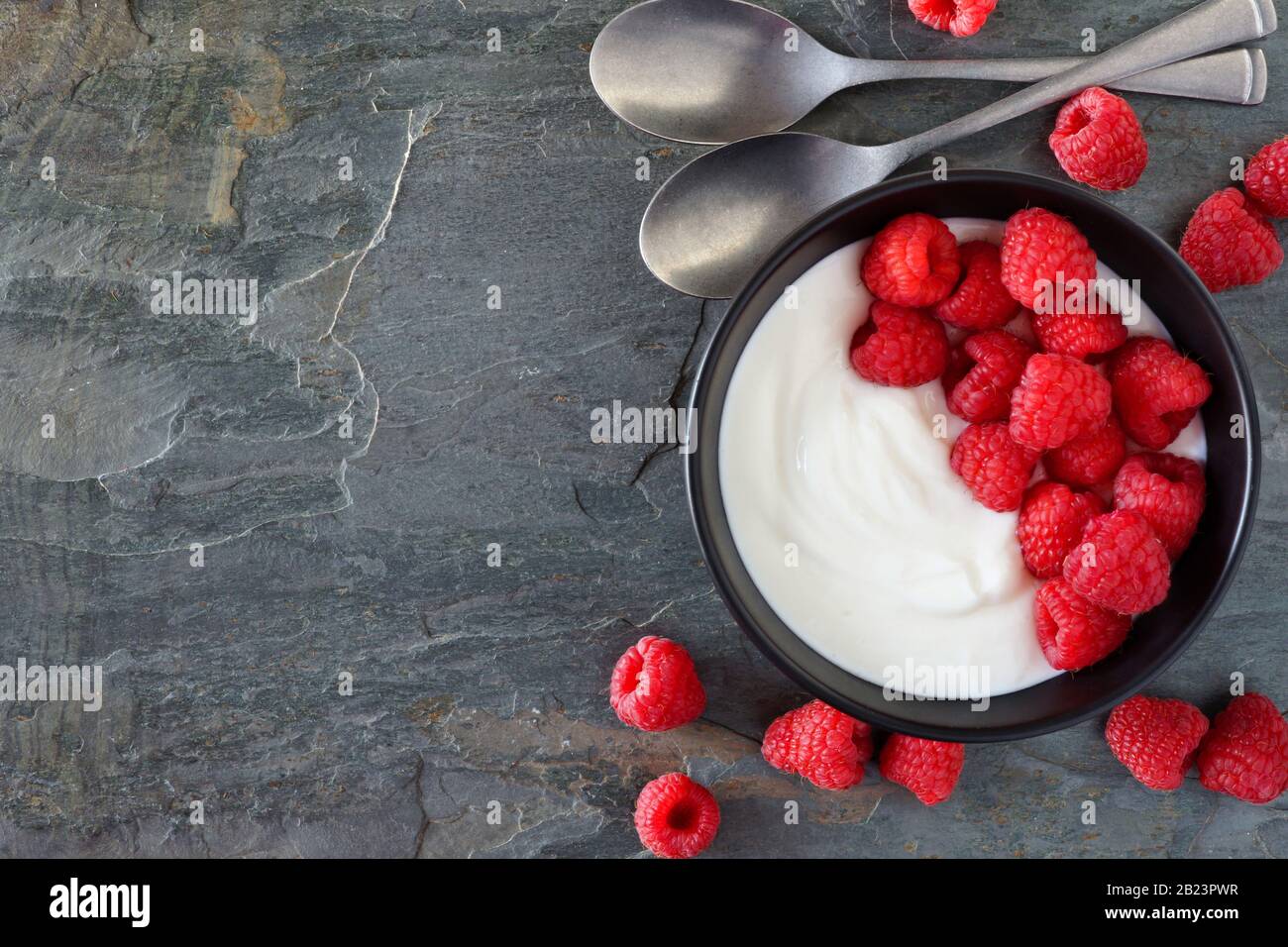 Ciotola di yogurt con lamponi. Vista dall'alto, bordo laterale su sfondo scuro in ardesia. Spazio di copia. Foto Stock