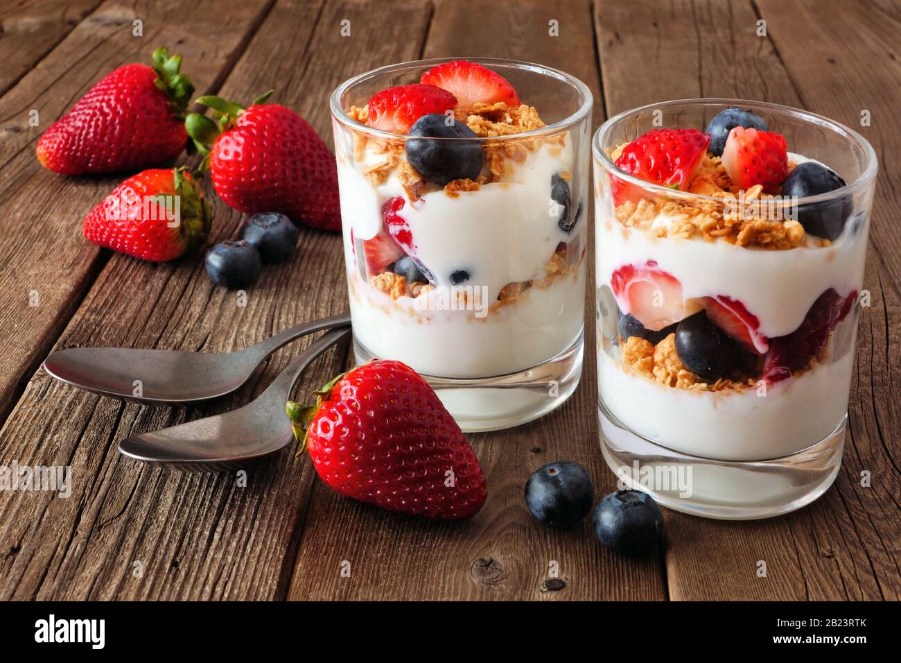 Parfaits fragola e mirtillo in bicchieri contro uno sfondo rustico di legno scuro Foto Stock
