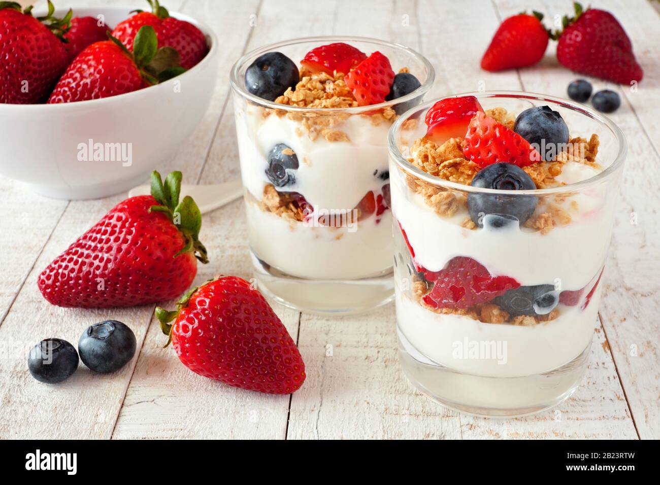 Parfaits di fragola e mirtillo in vetri contro uno sfondo di legno bianco luminoso Foto Stock