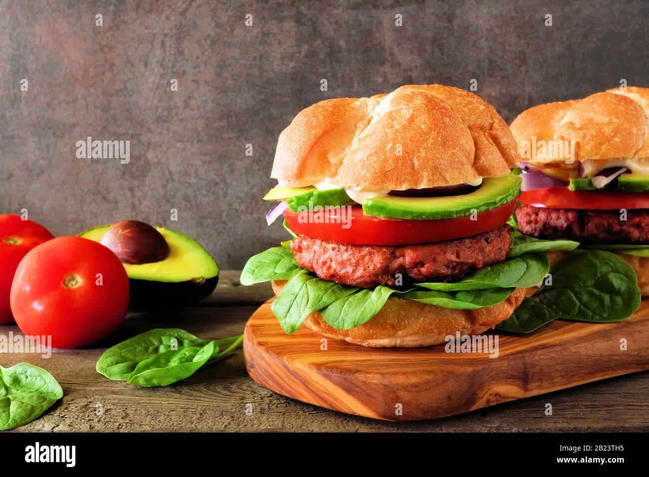 Hamburger senza carne a base di piante con avocado, pomodoro e spinaci su una tavola da portata su sfondo scuro Foto Stock