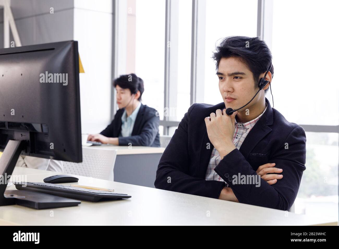 L'operatore asiatico attento del call center di sesso maschile considera i suoi progetti o incarichi nel computer dell'ufficio. Foto Stock