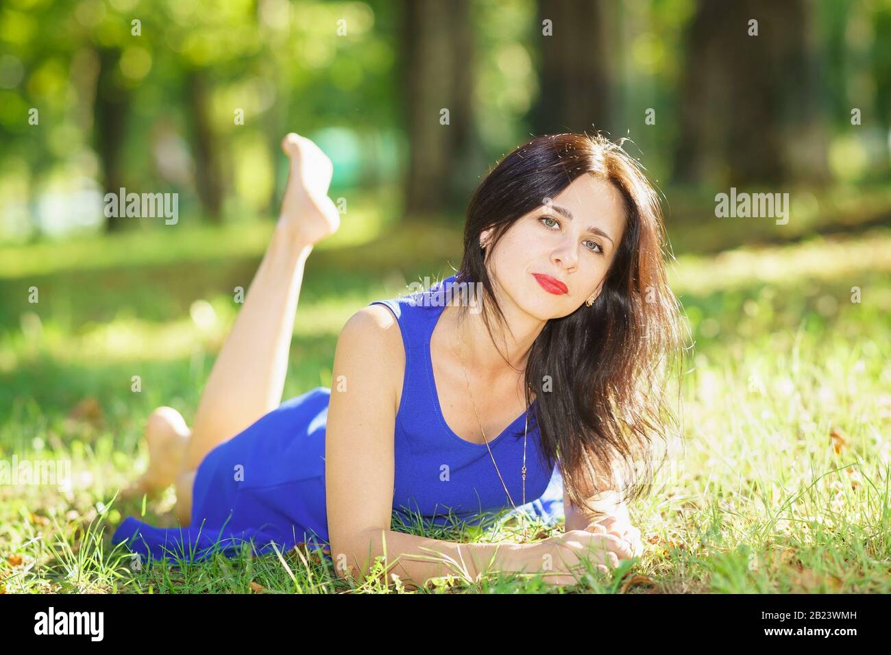 Bella giovane donna in abito blu sdraiata sull'erba. Buon umore Foto Stock