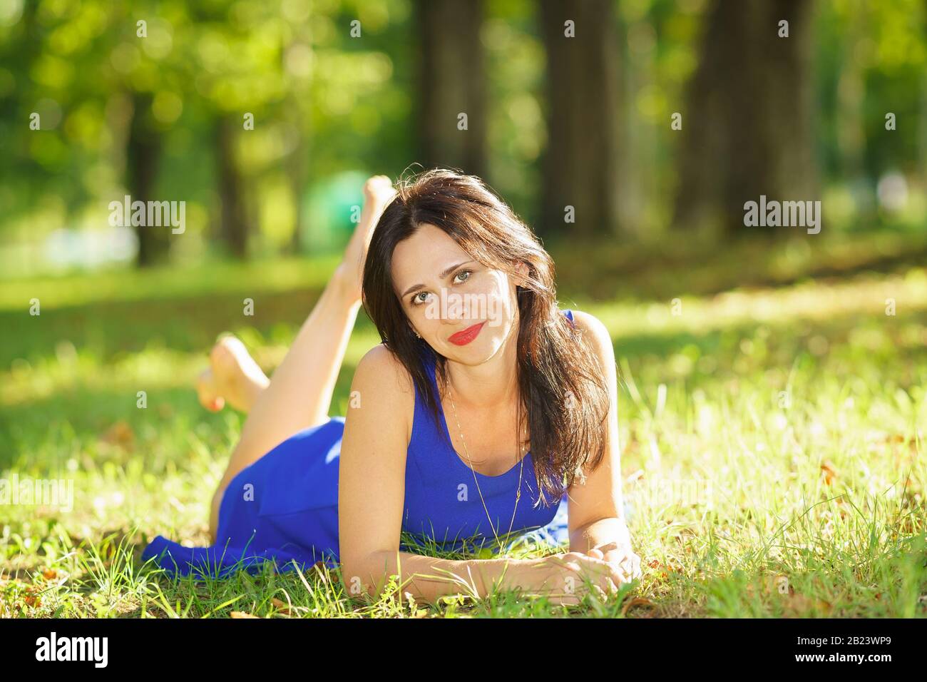 Bella giovane donna felice in abito blu sdraiata sull'erba. Buon umore Foto Stock