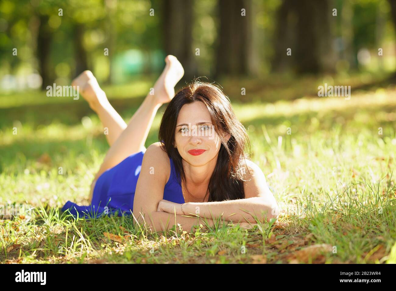 Bella giovane donna sorridente in abito blu sdraiata sull'erba. Buon umore Foto Stock