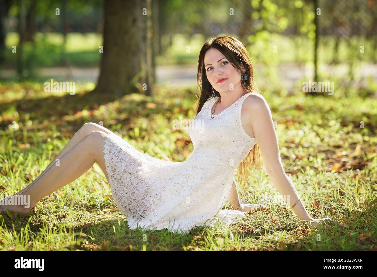 Bella ragazza felice in abito bianco seduto sull'erba. Buon umore Foto Stock