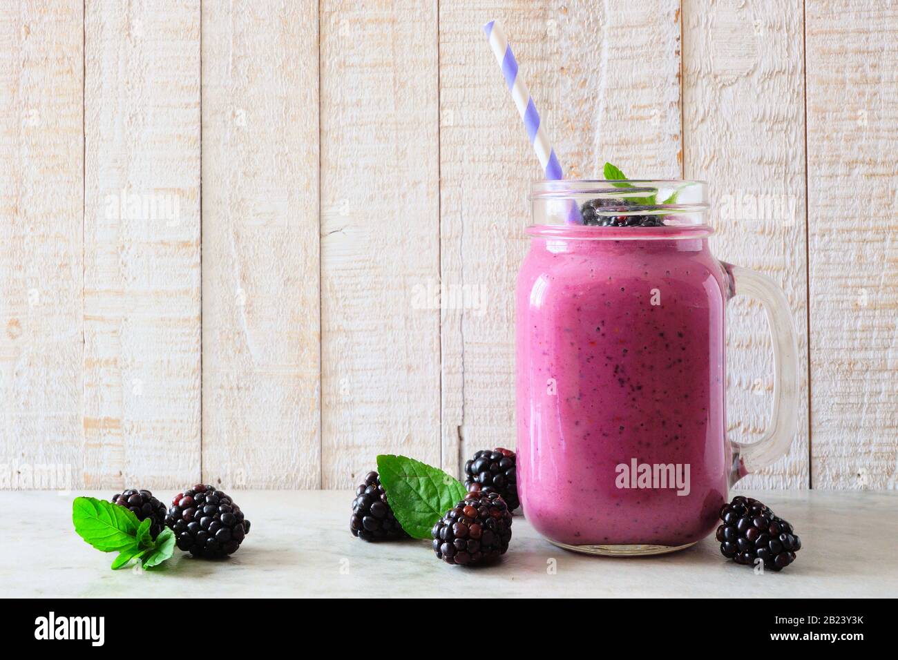 Frullato BlackBerry in un bicchiere da muratore con frutti di bosco sparsi su uno sfondo rustico in legno bianco Foto Stock