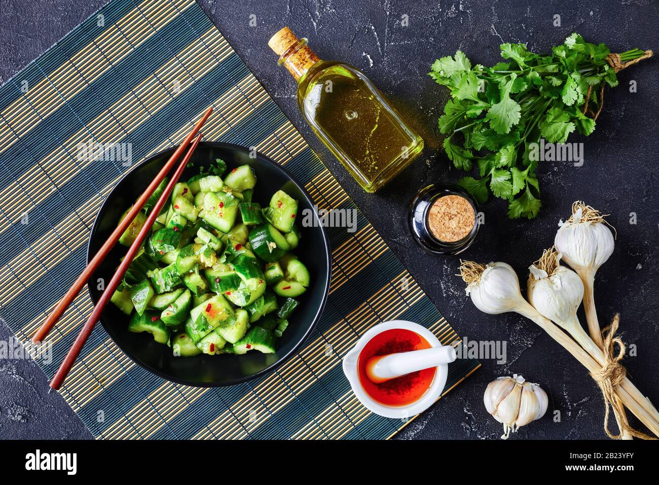 Insalata cinese di cetrioli Fracassati, pai huang gua, con salsa di soia all'olio di sesamo al peperoncino, cosparsa di foglie fresche di coriandolo in una ciotola nera o Foto Stock