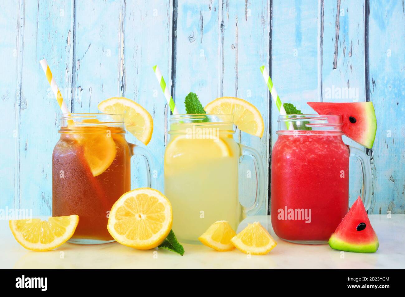 Varietà di bevande estive in bicchieri da vasetto mason con frutta su sfondo di legno blu. Tè freddo, limonata e succo di cocomero. Foto Stock