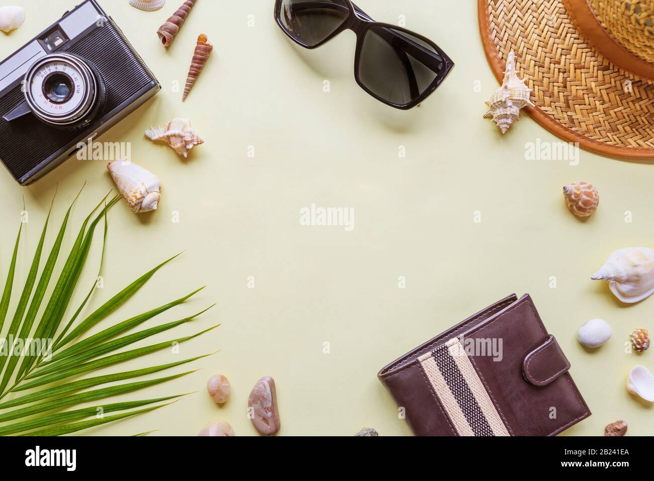 Accessori uomo viaggiatore: Verde foglia di palma tropicale, foto fotocamera, conchiglie e occhiali da sole sono su sfondo giallo con copia-spazio. Vista dall'alto del viaggio Foto Stock