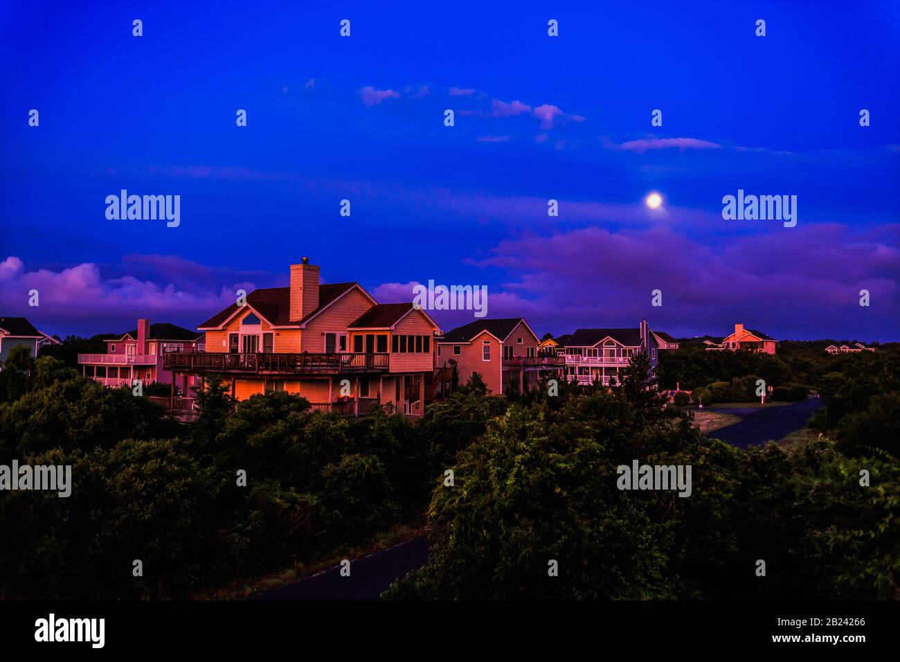 I primi raggi di luce dell'alba sulle case di vacanza costiere contro un cielo e la luna di notte sbiadimento. Foto Stock