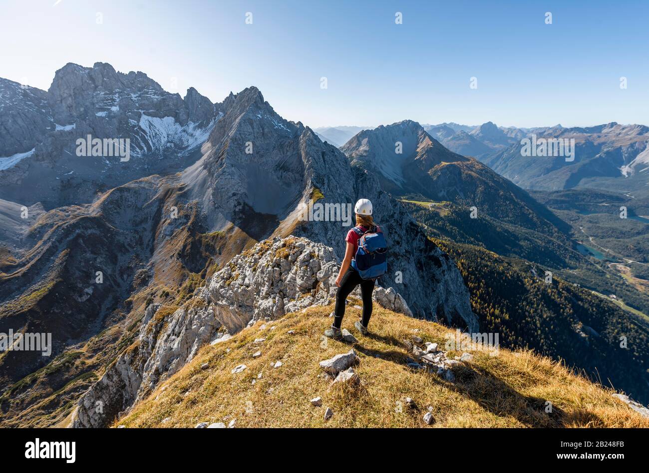 Giovane donna, alpinista con casco da arrampicata guardando il paesaggio di montagna, escursione a Ehrwalder Sonnenspitze, dietro Gruenstein e ovest Foto Stock