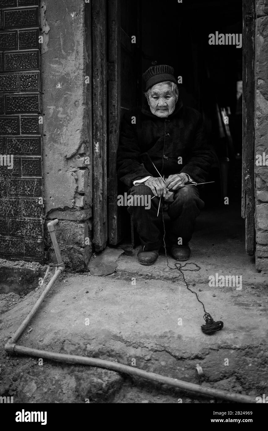 Scena di strada in un quartiere della città vecchia di Chongqing. Vecchia donna nella sua porta di fronte, questi quartieri sono gradualmente in fase di demolizione per fare spazio per Foto Stock