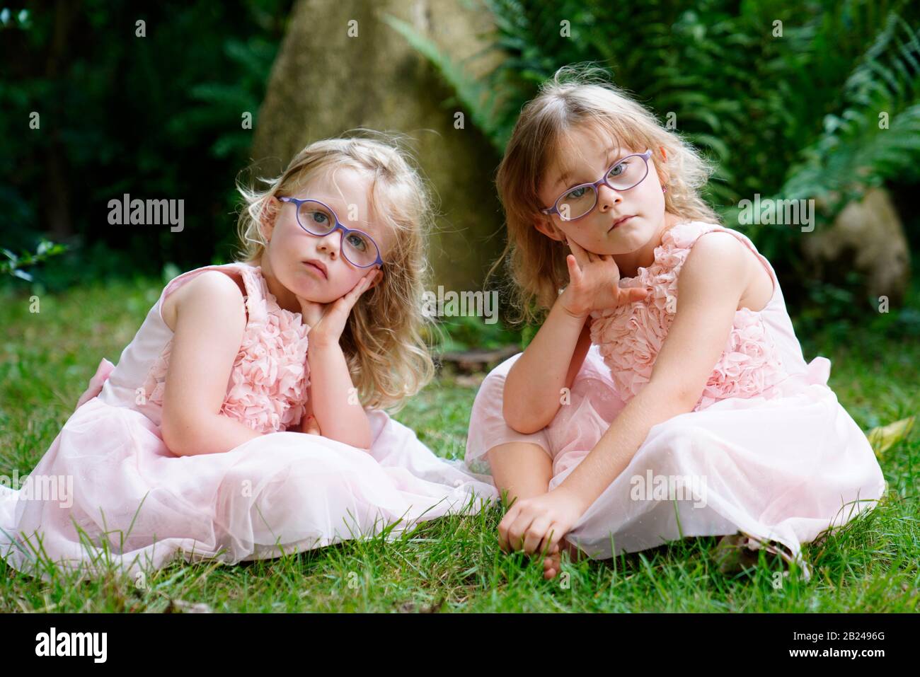 Due sorelle in abito rosa seduti nel giardino (6 anni, 3 anni) Repubblica Ceca Foto Stock