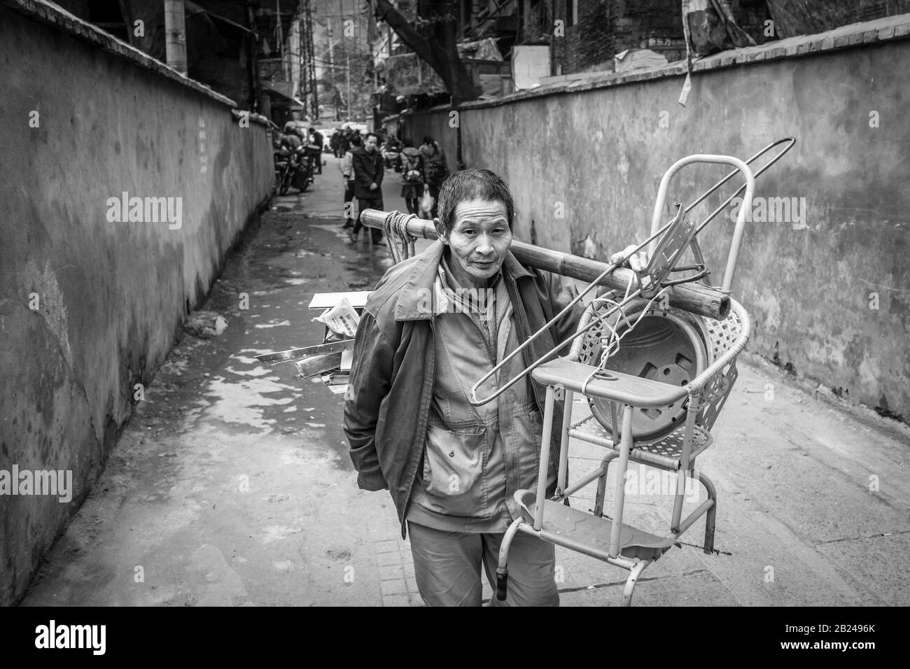 Scena di strada in un quartiere della città vecchia di Chongqing. Una donna con i suoi mobili esce dal suo appartamento, Chongqing, Cina Foto Stock