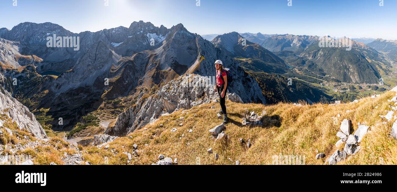 Giovane donna, alpinista con casco da arrampicata guardando il paesaggio di montagna, escursione a Ehrwalder Sonnenspitze, dietro Gruenstein e ovest Foto Stock