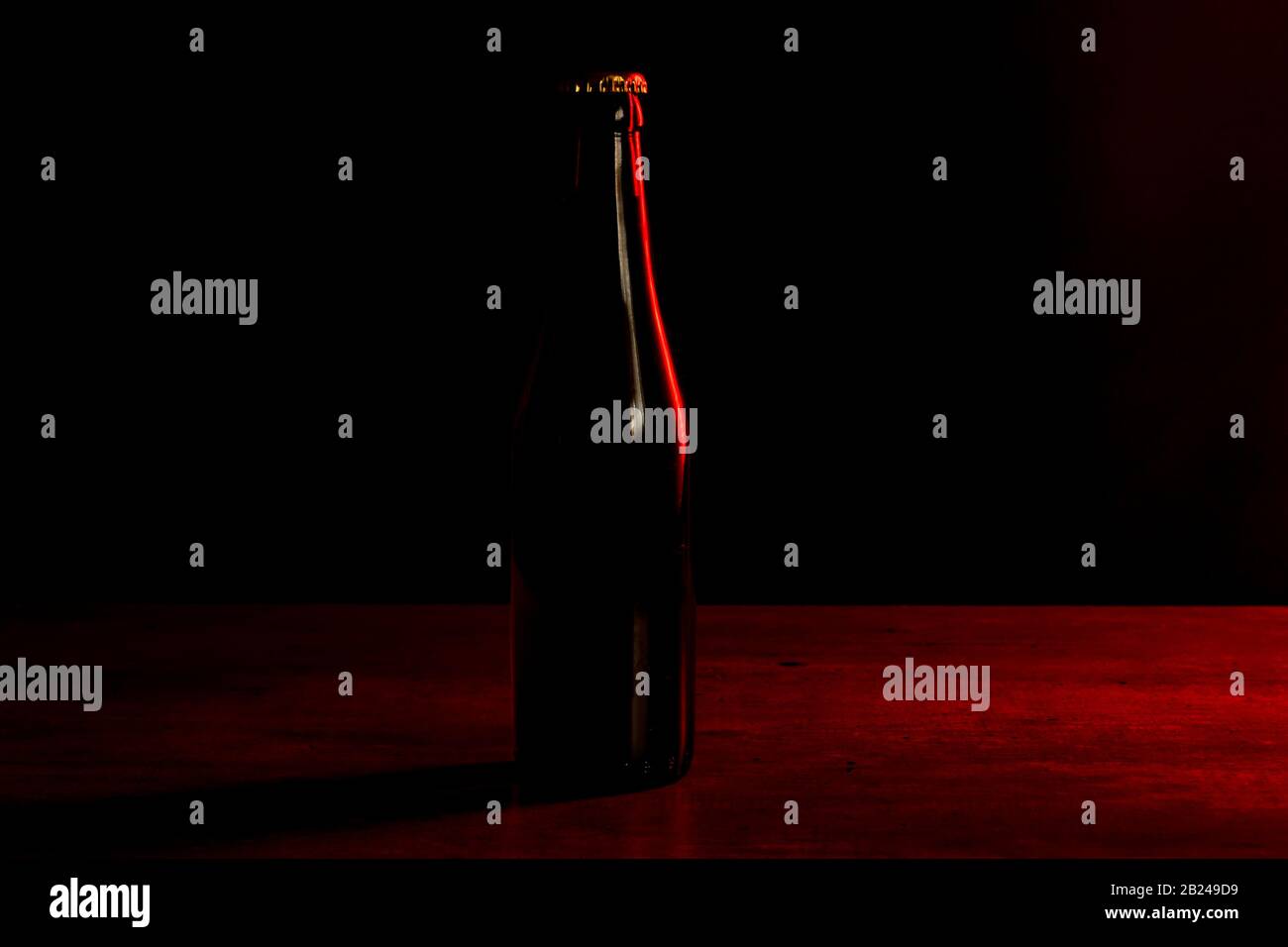 silhouette di una bottiglia di birra su sfondo nero con luci rosse che la illuminano da un lato. Foto Stock