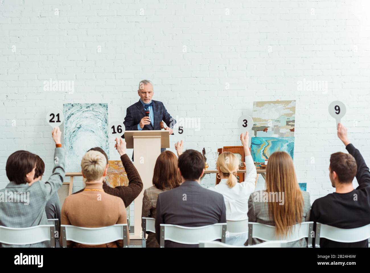 auctioneer parlare con il microfono e guardare gli acquirenti con le pale d'asta durante l'asta Foto Stock