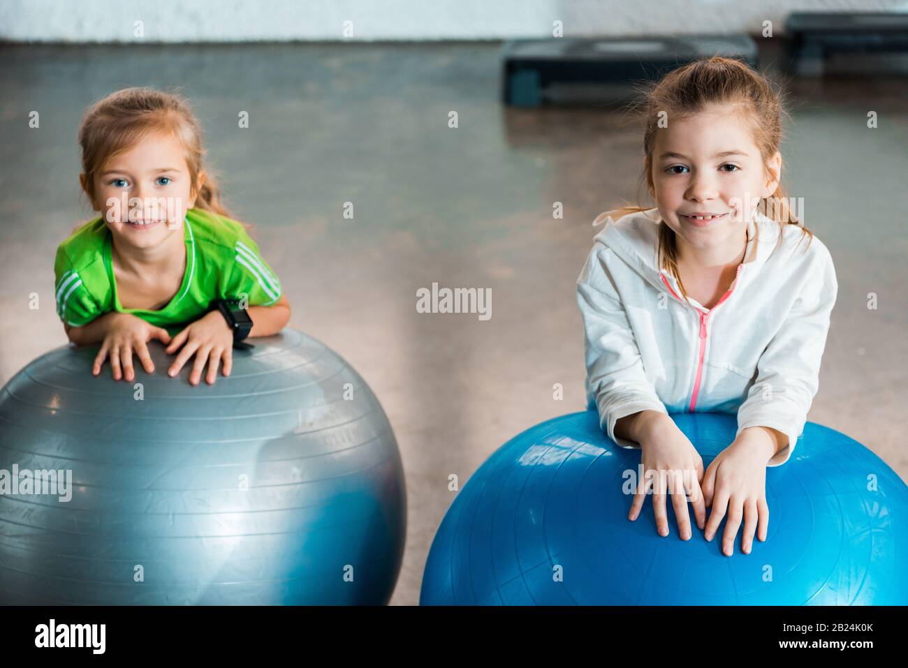 Fuoco selettivo dei bambini che guardano la macchina fotografica, sorridente ed appoggiandosi sulle sfere di idoneità in palestra Foto Stock