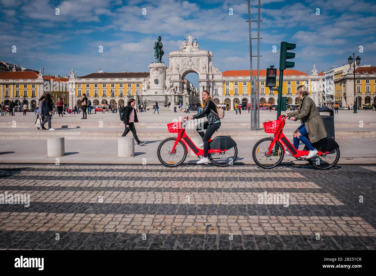 Due ciclisti donne in bicicletta di fronte alla piazza commerciale di Lisbona durante il giorno Foto Stock