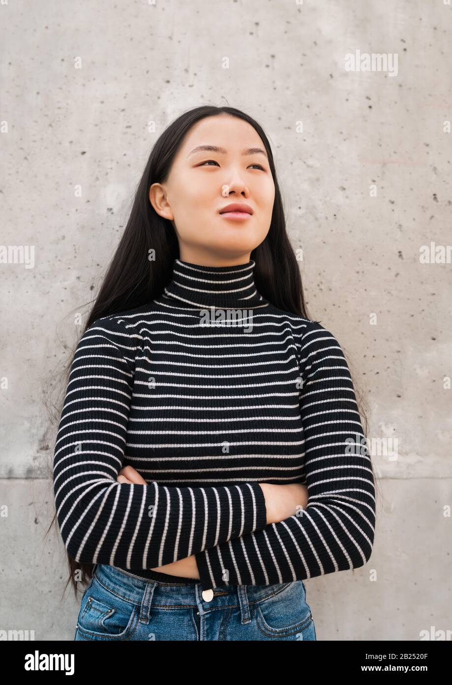 Ritratto di giovane bella donna asiatica in piedi all'esterno contro la parete grigia. Foto Stock